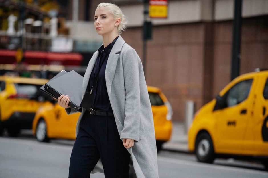 Side view contemplative businesswoman in formal clothes carrying document folder and crossing busy road in downtown