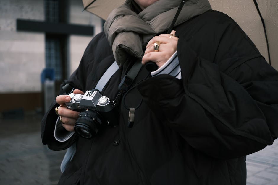 A person holding a vintage camera under an umbrella on a rainy day, capturing urban moments.