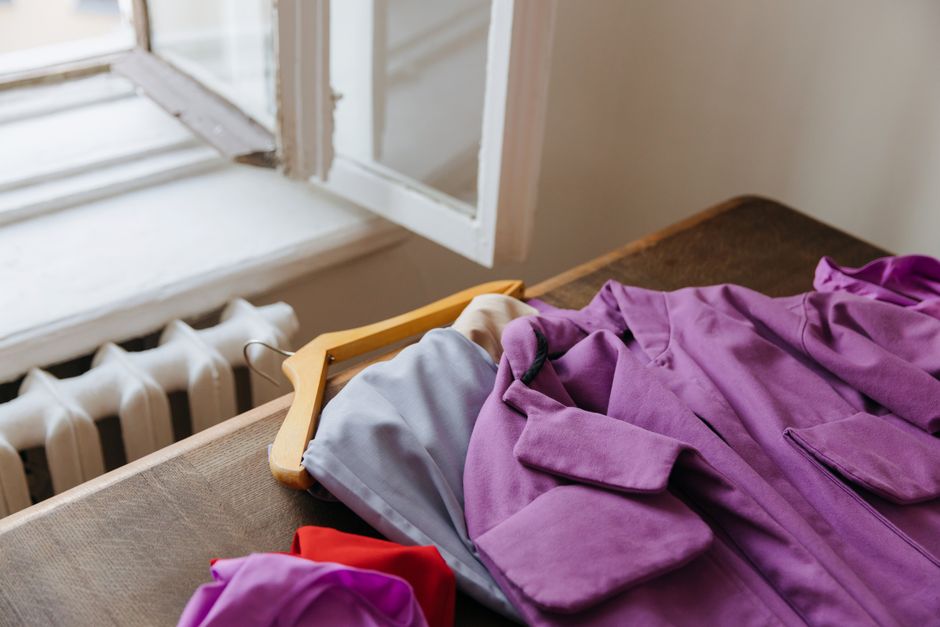 Purple coat on hanger beside open window, offering natural light and warmth.