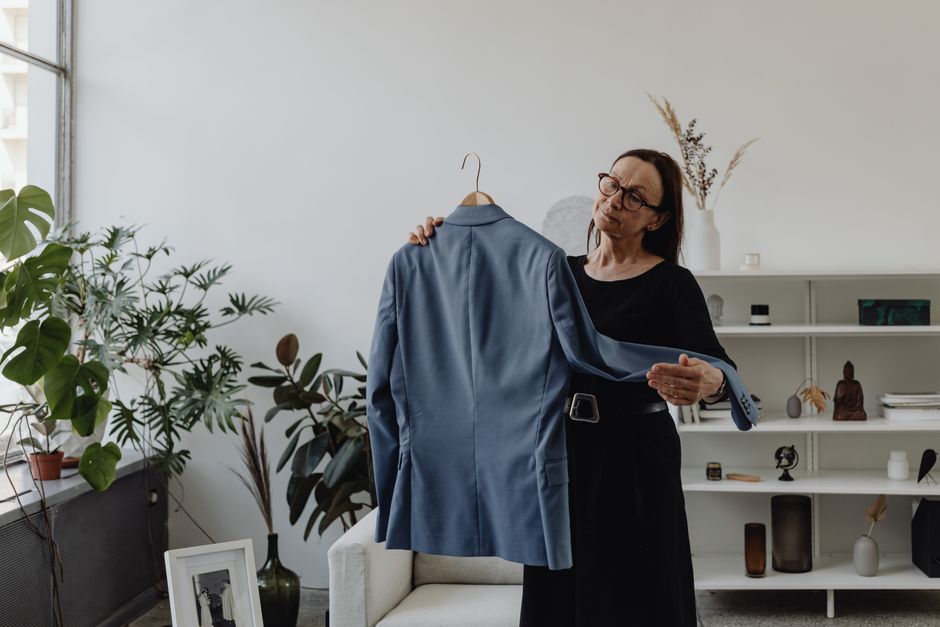 A thoughtful woman holding a blue jacket in her stylish living room, surrounded by plants and decor.