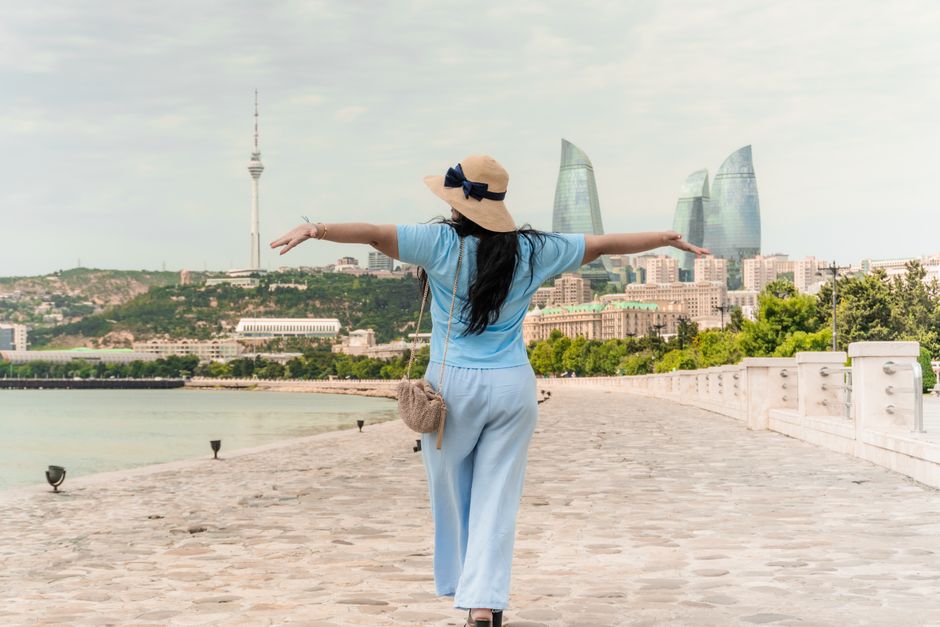 A woman in summer attire joyfully walks along a promenade in Baku with the Flame Towers in sight.