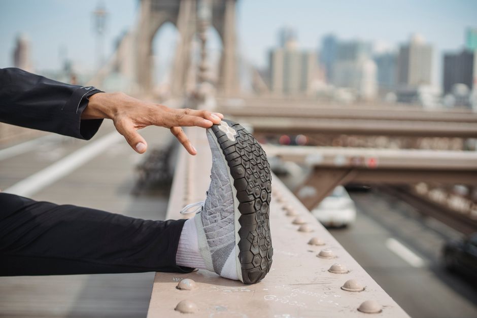 Person stretching on Brooklyn Bridge, focusing on foot with city skyline in background.