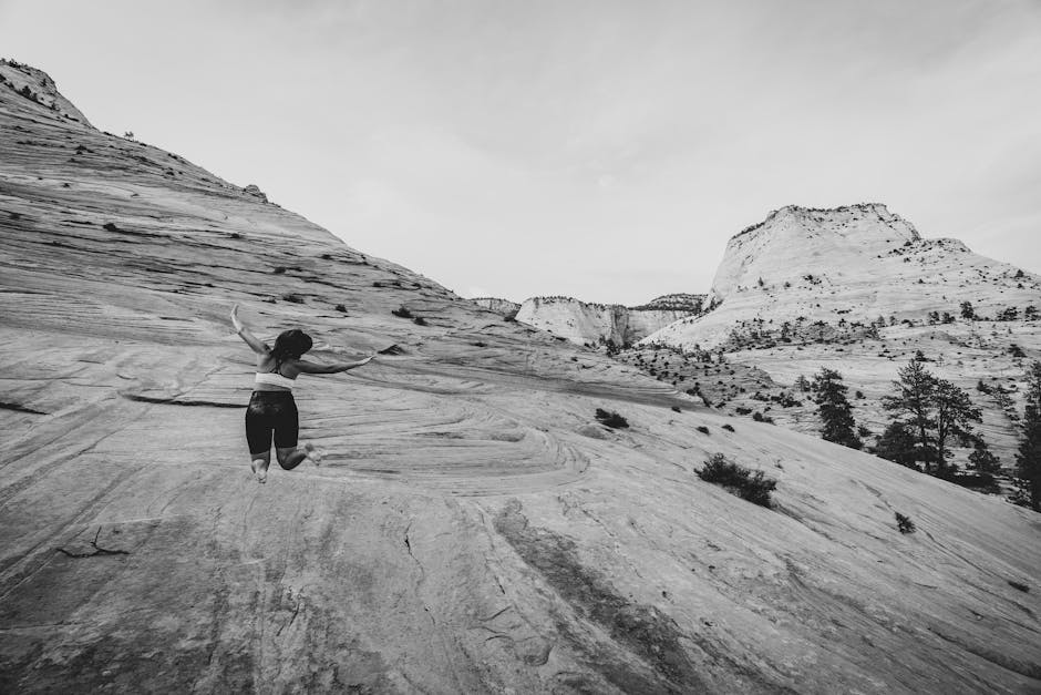 Black and white photograph of a woman embracing nature amidst a stunning desert landscape, conveying freedom.