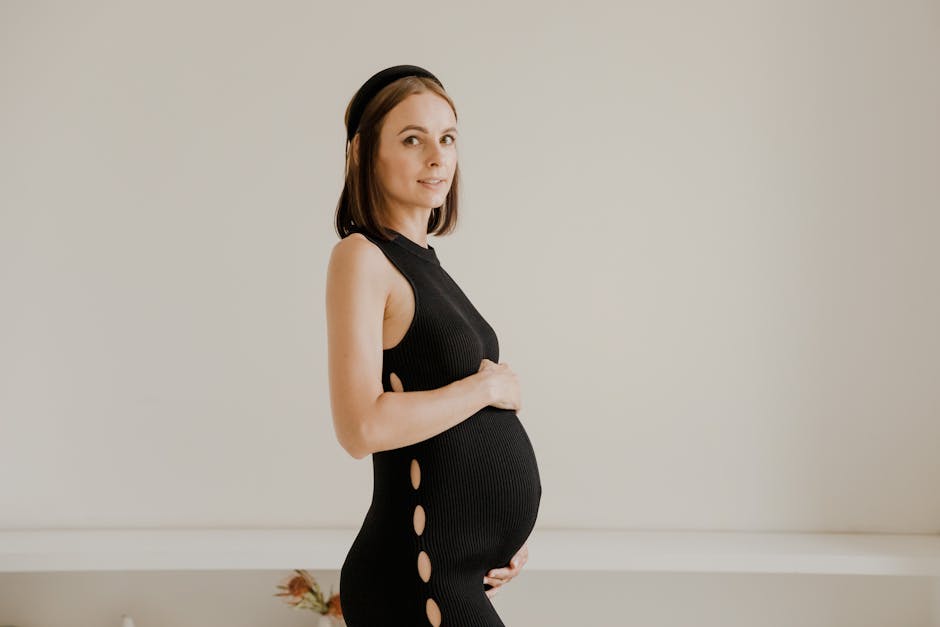 Minimalist portrait of a pregnant woman posing gracefully in a black dress indoors.