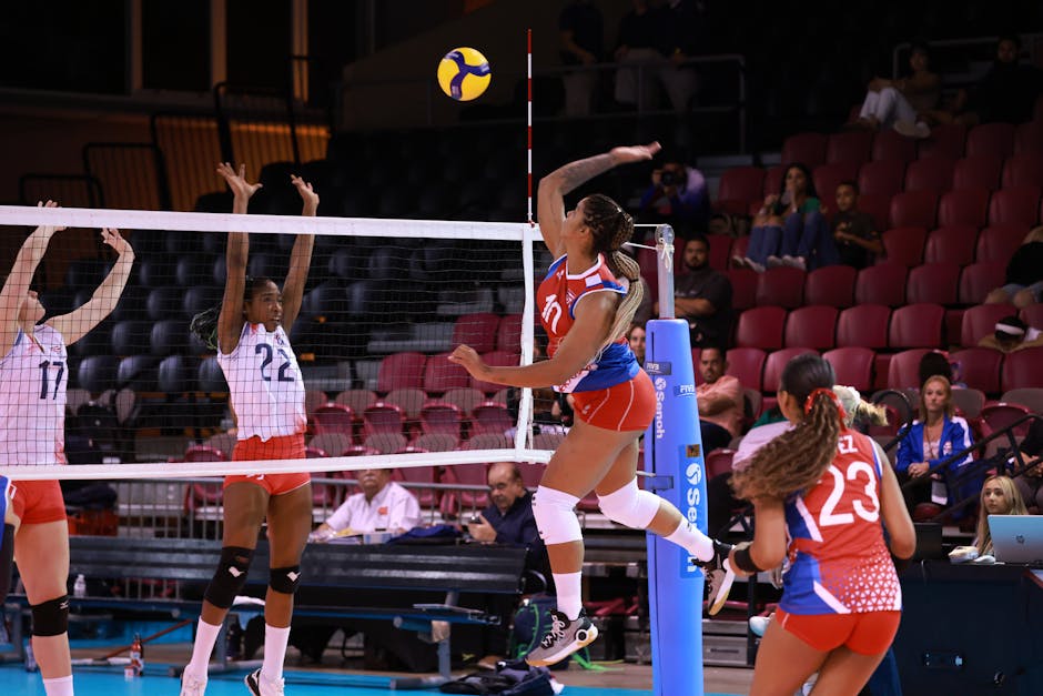 Dynamic action shot from a women's volleyball match with players in mid-air at the net.
