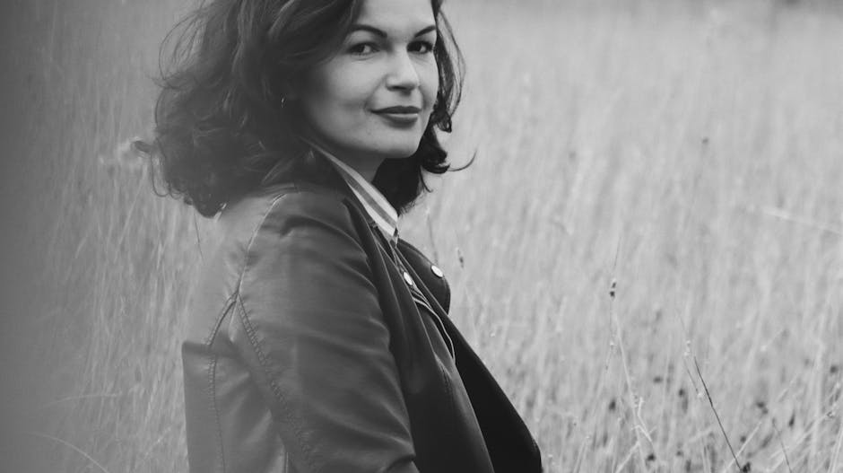 Artistic black and white portrait of a woman sitting outdoors in a serene field.