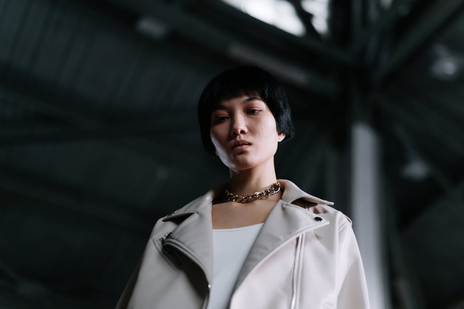 Low angle portrait of a woman with black hair and chain necklace, exuding confidence in an industrial setting.
