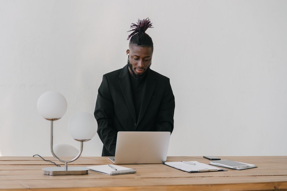 A businessman in a black suit works intently on his laptop at an indoor desk.