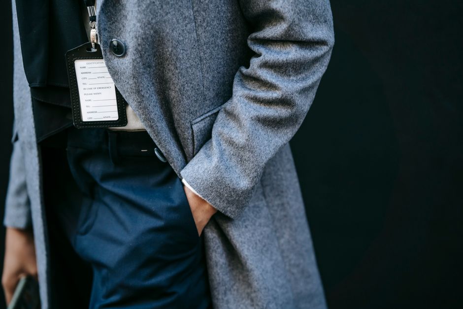 Crop anonymous female entrepreneur in elegant coat and name tag walking on city street with hand in pocket