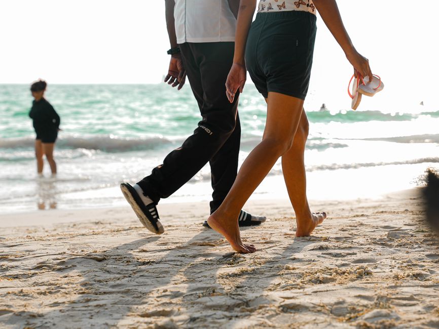 A couple walks barefoot on a sunny beach, enjoying a relaxing seaside day.