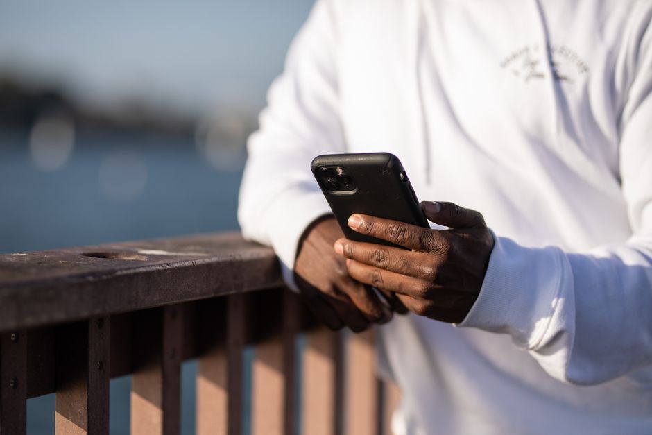 A person in a white hoodie using a smartphone on a wooden railing by the water.