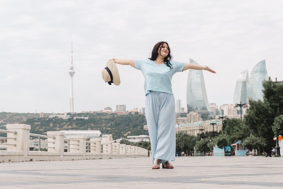Woman enjoying a breezy day in Baku, Azerbaijan, with iconic landmarks in the background.