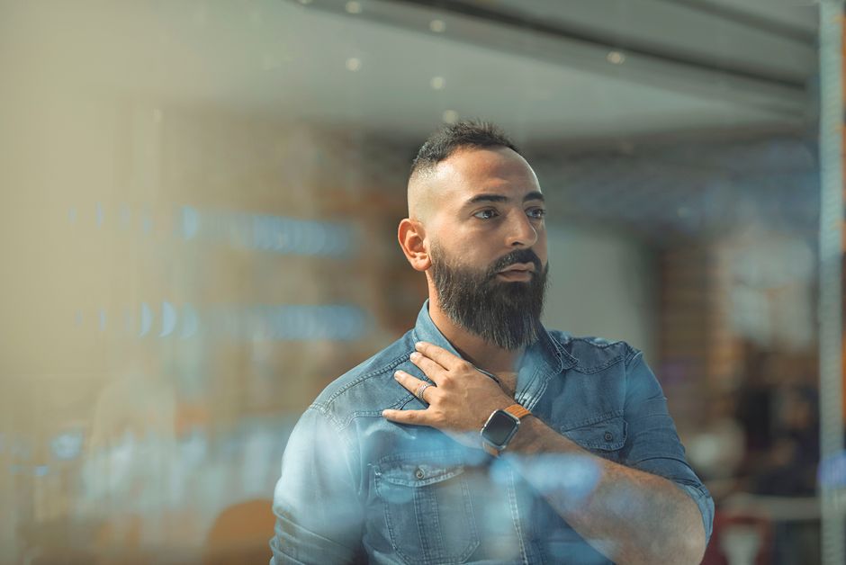 A thoughtful bearded man in casual attire with a smartwatch in a modern indoor environment.