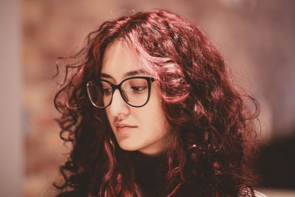 Young woman with curly red hair and glasses in a thoughtful pose.
