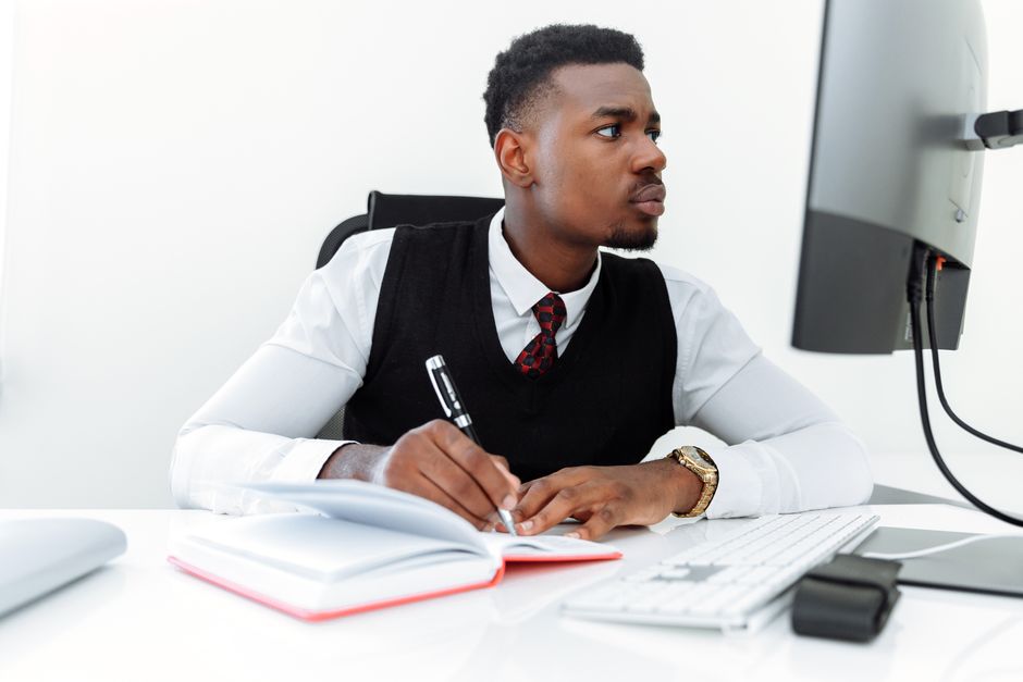 Professional businessman writing notes while working on a computer in a modern office.