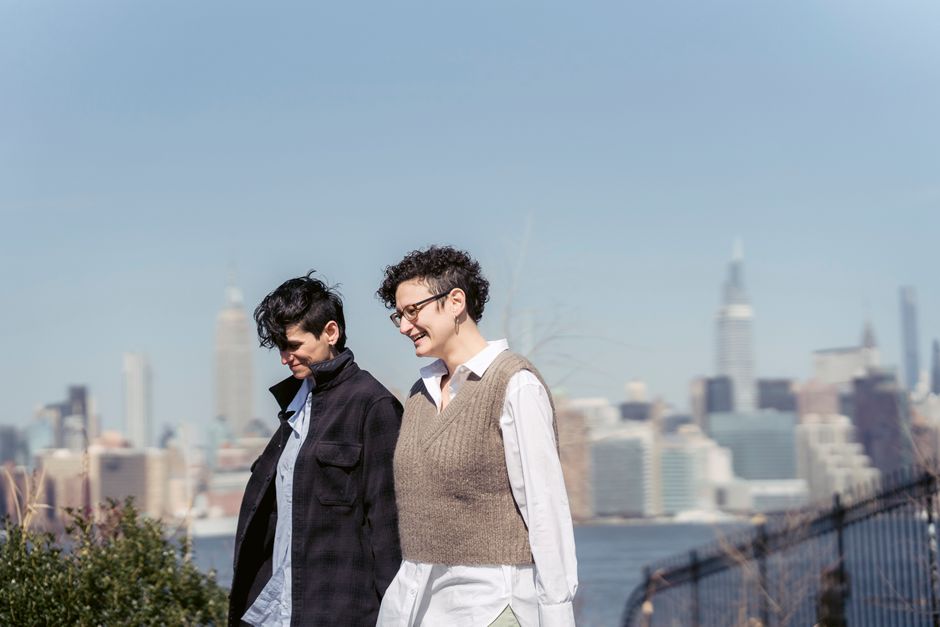 Cheerful best female friends speaking against river and buildings under blue sky in sunny city