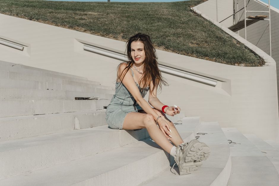 A woman in a denim outfit sits on white concrete stairs under the sun.