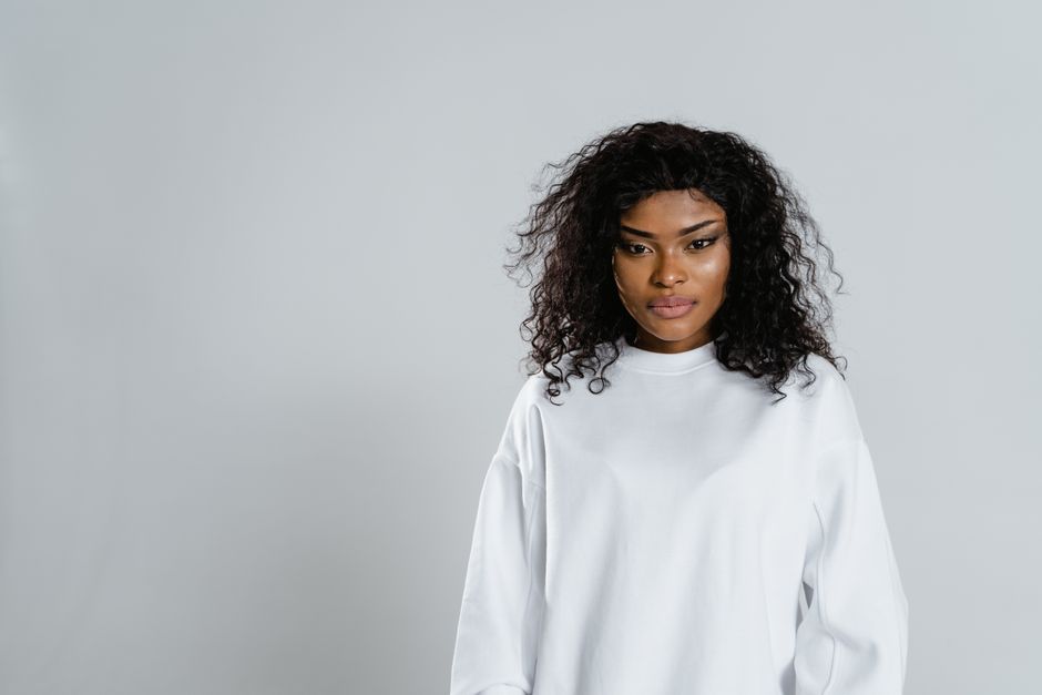 Studio portrait of a serious African American woman in white sweater, looking directly at camera.