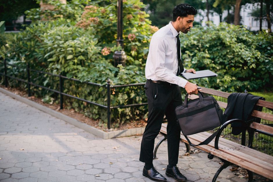 Professional male in business attire working with a laptop on a park bench.