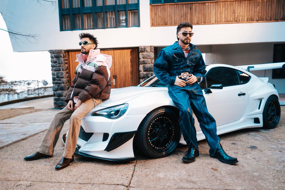 Two stylish men in trendy outfits posing with a white sports car outside a modern building.