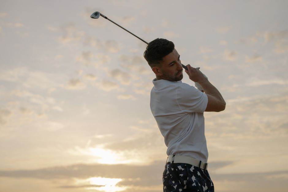 Professional golfer in action, swinging club with sunset backdrop.