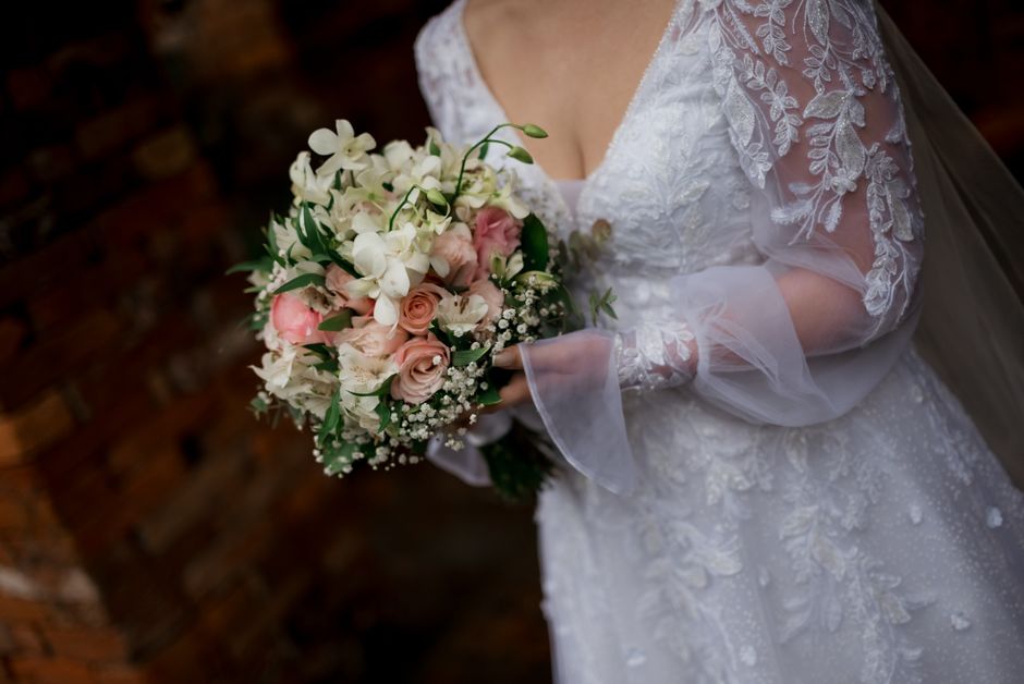 A close-up of a bride in a lace wedding dress holding a beautiful bouquet of roses and lilies.