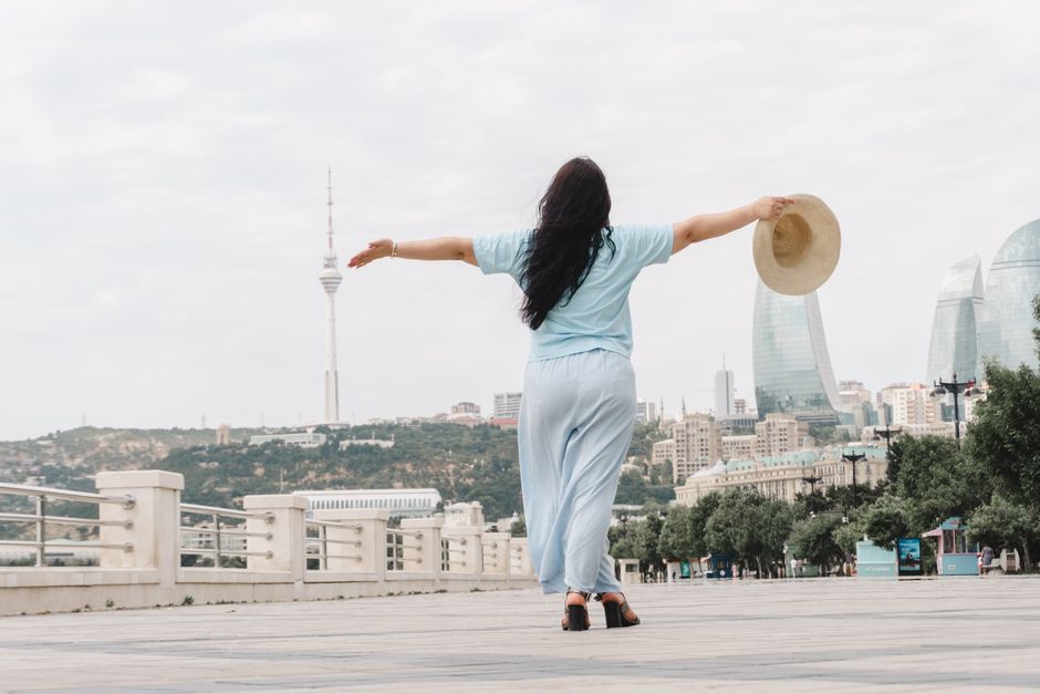 A woman enjoys the freedom as she strolls on Baku's promenade with landmarks in view.