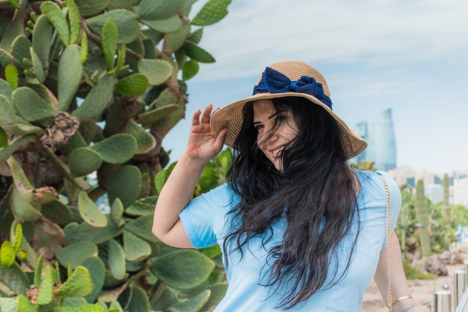 Happy woman in straw hat explores Baku's iconic Flame Towers and cactus garden.