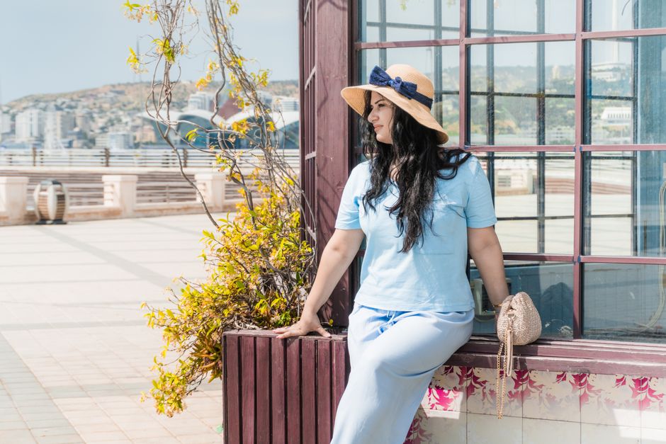 Woman in straw hat relaxing by the waterfront in Baku, enjoying a sunny day.