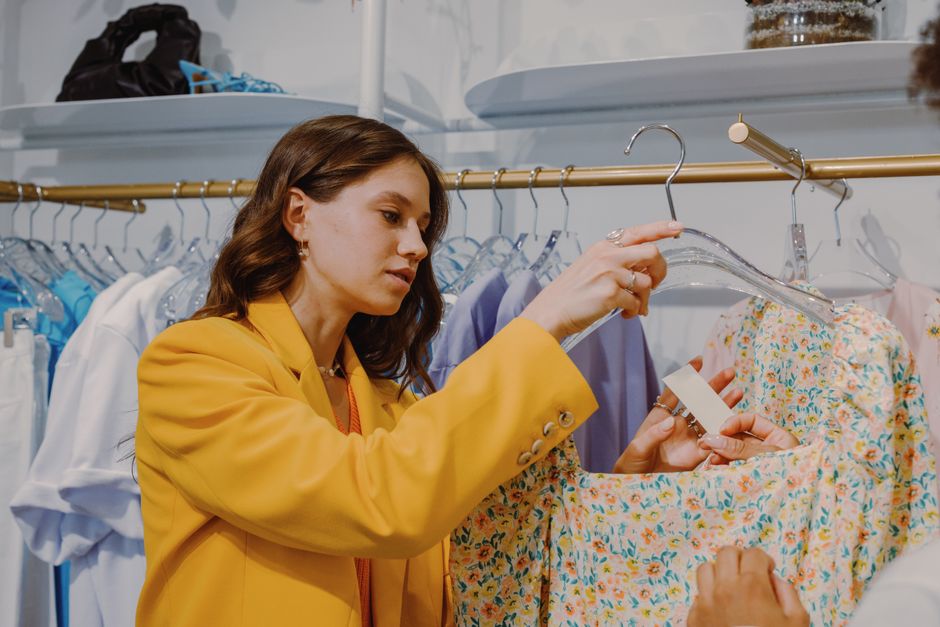 Fashionable woman explores clothing options in a boutique, focusing on a floral dress.