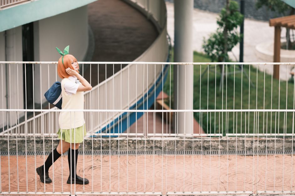 A young woman in cosplay attire walking along a path outdoors, surrounded by greenery.