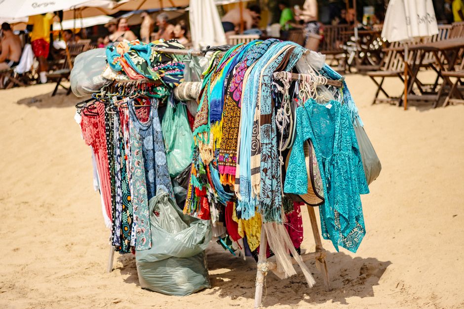 Vibrant clothing stand on beach showcasing colorful garments with sandy background.