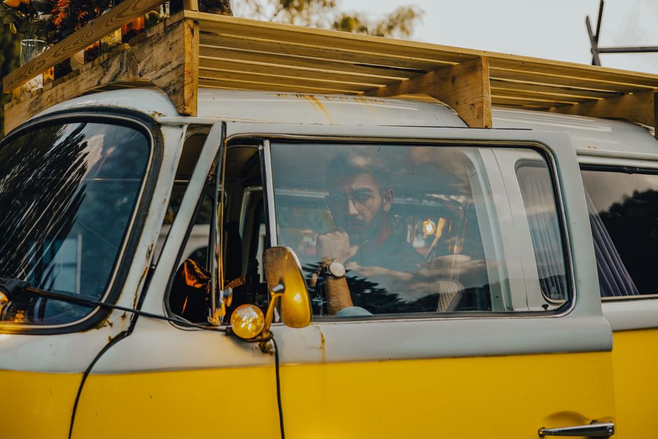 A man drives an old yellow van during a sunny day, capturing a retro travel vibe.