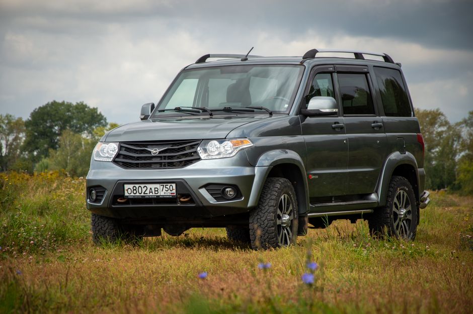 Silver UAZ SUV parked in a scenic rural meadow, showcasing rugged design.