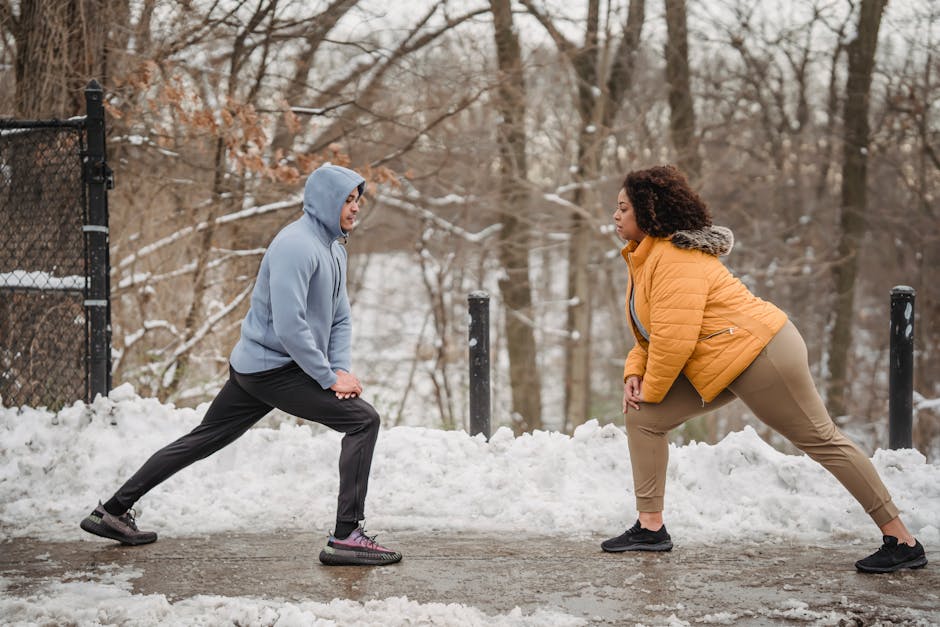 Full body side view of plus size African American female with black personal coach doing stretching exercise while standing on snowy path in park