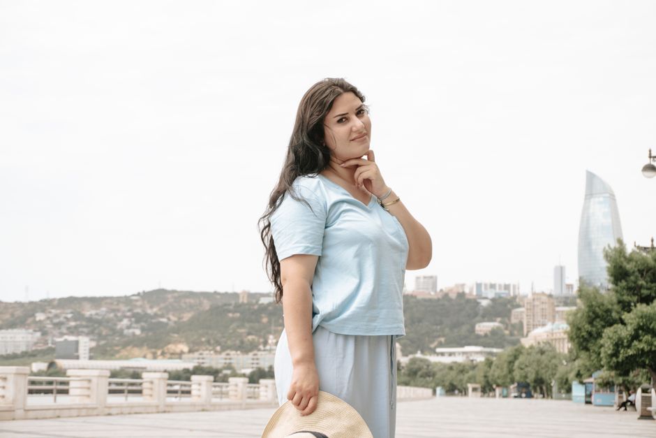Portrait of a woman in casual attire posing outdoors with Baku skyline in background.