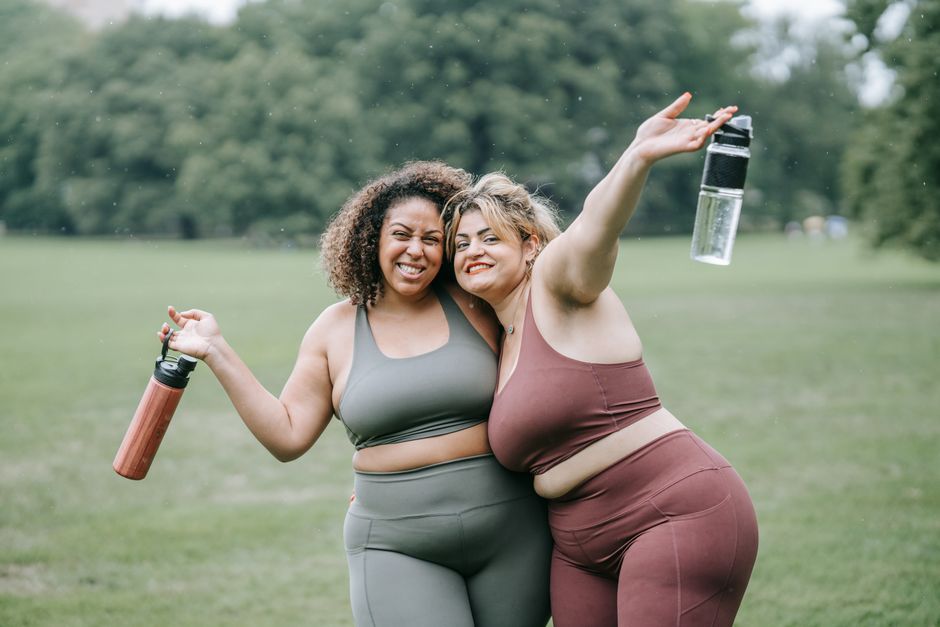 Two women in sportswear smiling and hugging outdoors, holding water bottles.
